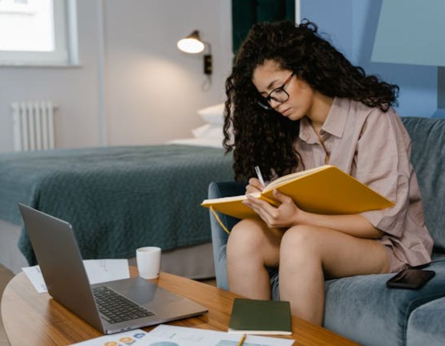 a young lady scribbling down some notes from a laptop
