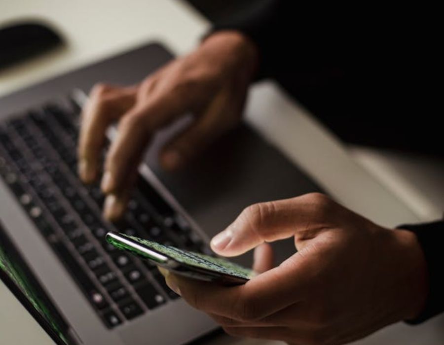 A person using a phone while typing on a laptop