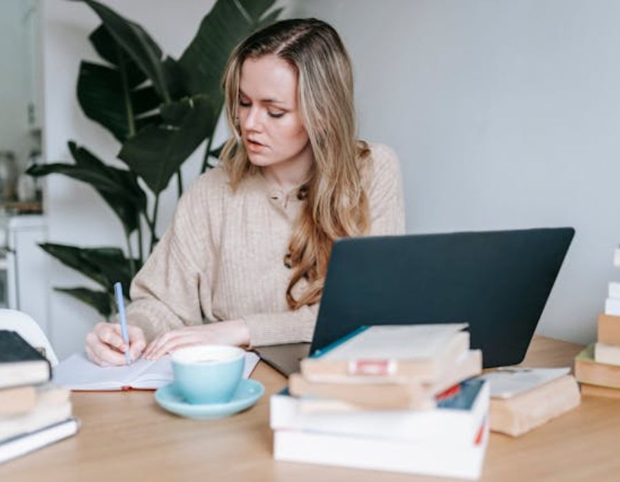 A woman writing information in notebook near laptop and coffee