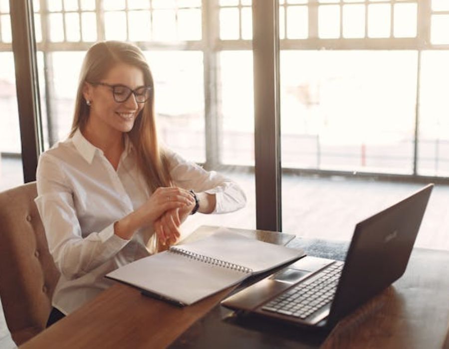 a woman using a laptop while looking at her watch