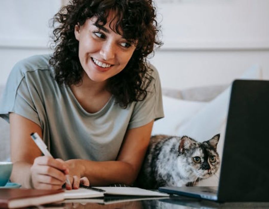 a woman writing down something while using a laptop